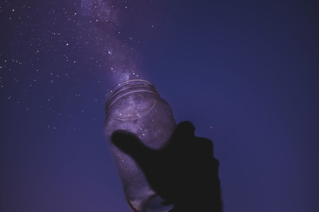A transparent jar from which shiny dust flies towards the night sky.